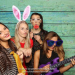 4 Mädchen fotografieren sich mit Luftgitarre und Hasenohren vor einer Fotobox